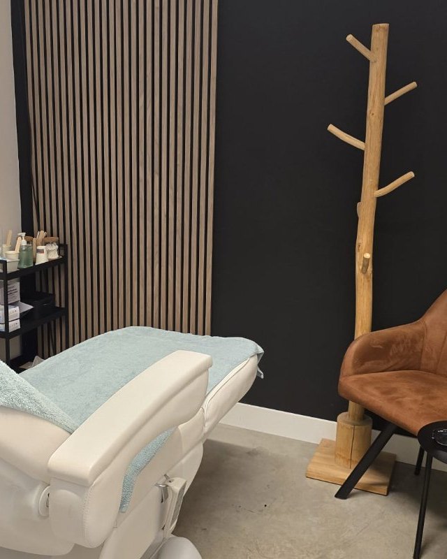 De behandelkamer met de laser, de lamellenwand, een cognackleurige fauteuil en een houten kapstok